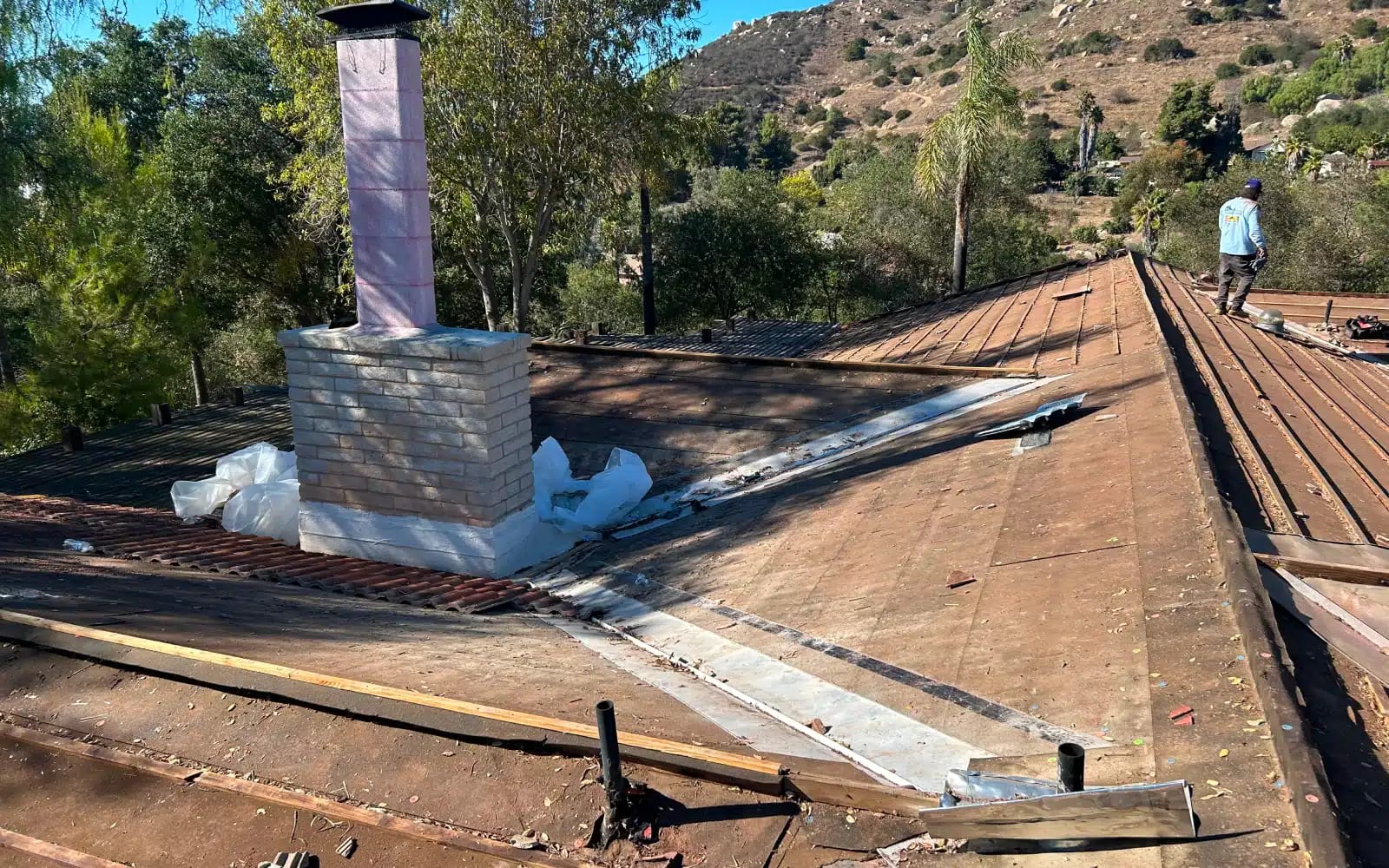 Concrete tile roof tear-off in San Marcos, California, showing exposed roof deck and chimney area during full roof replacement.